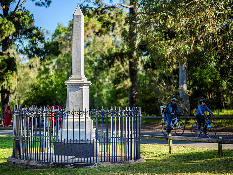 People riding bikes in park with statue in foreground