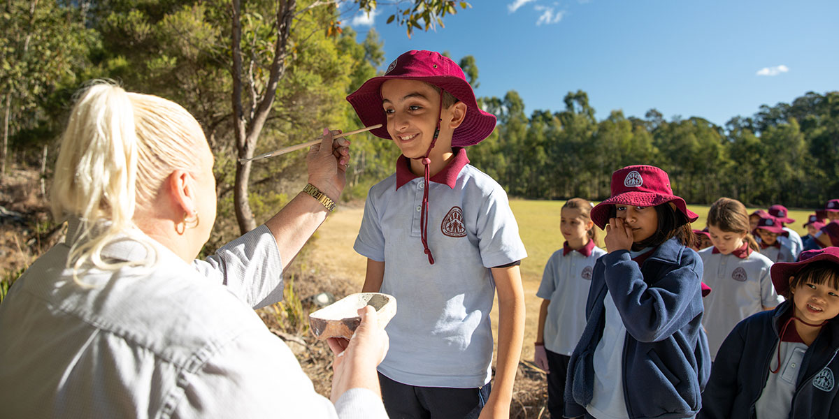 Teacher painting school child's face in parkland