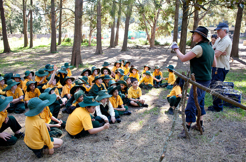 Teacher giving lesson to group of school children in parklands