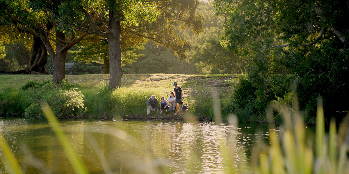 Family sitting on the edge of a lake in parklands