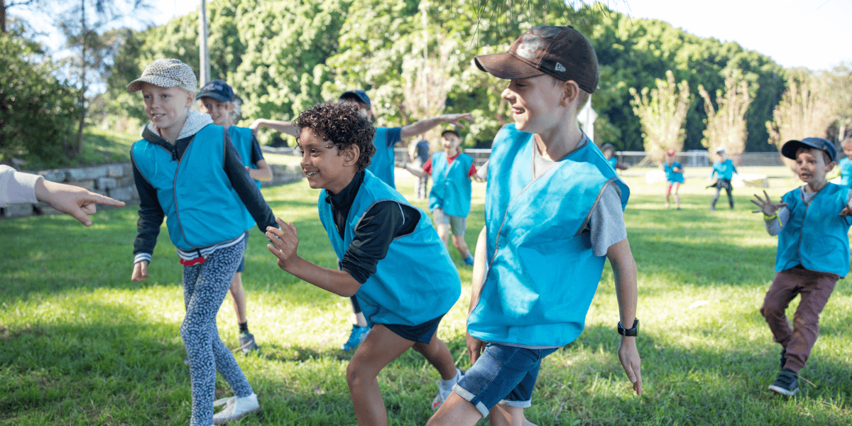 A group of four young children wearing blue vests race one another in a green park