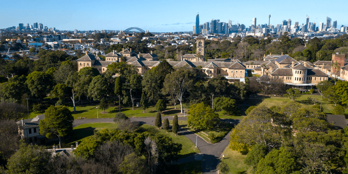 An aerial view over Callan Park with the Kirkbride building in the foreground, and Sydney city skyline in the background.