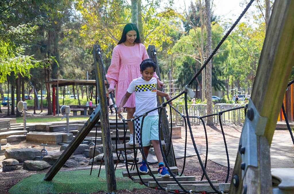 A woman and a child carefully walk together on a rope bridge.