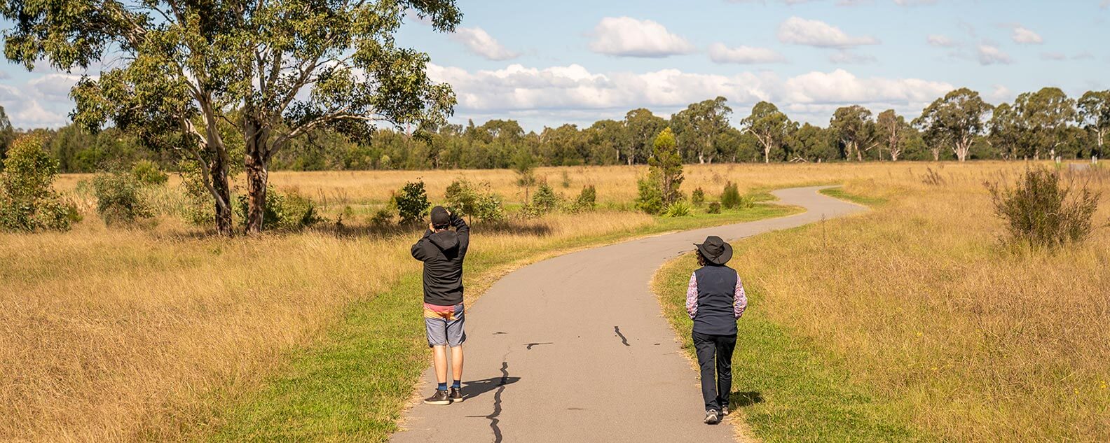 A pair of walkers on a path in a field, surrounded by nature on the Plough and Harrow Loop trail.