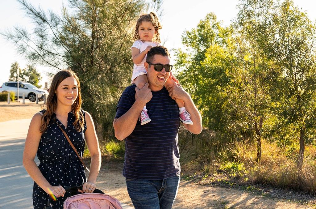 A couple with their baby walks on the Lizard Log Kids Trail, guiding a stroller.