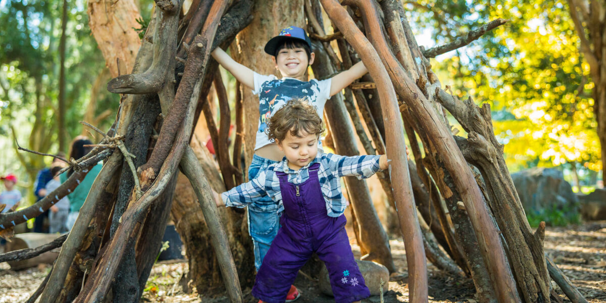 Two kids playing in a stick cubby house