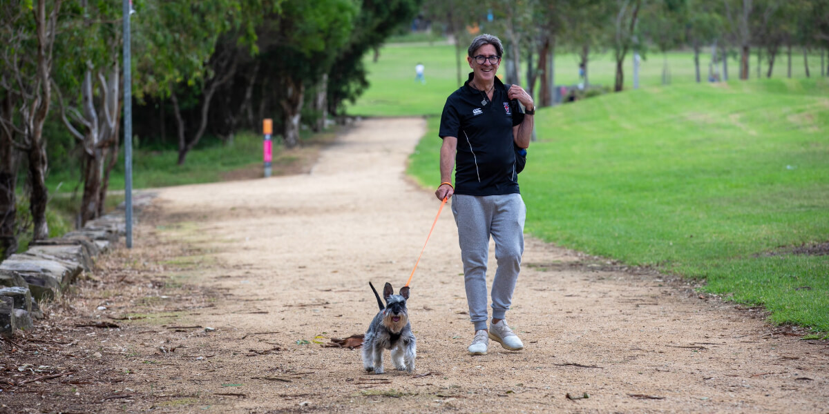 A man walking with his small dog on the footpath at Plough and Harrow Loop
