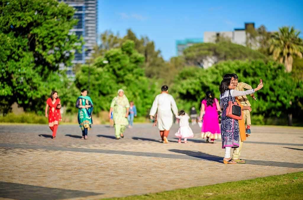 A diverse group of people strolls together through a sunny park, enjoying nature and each other's company.