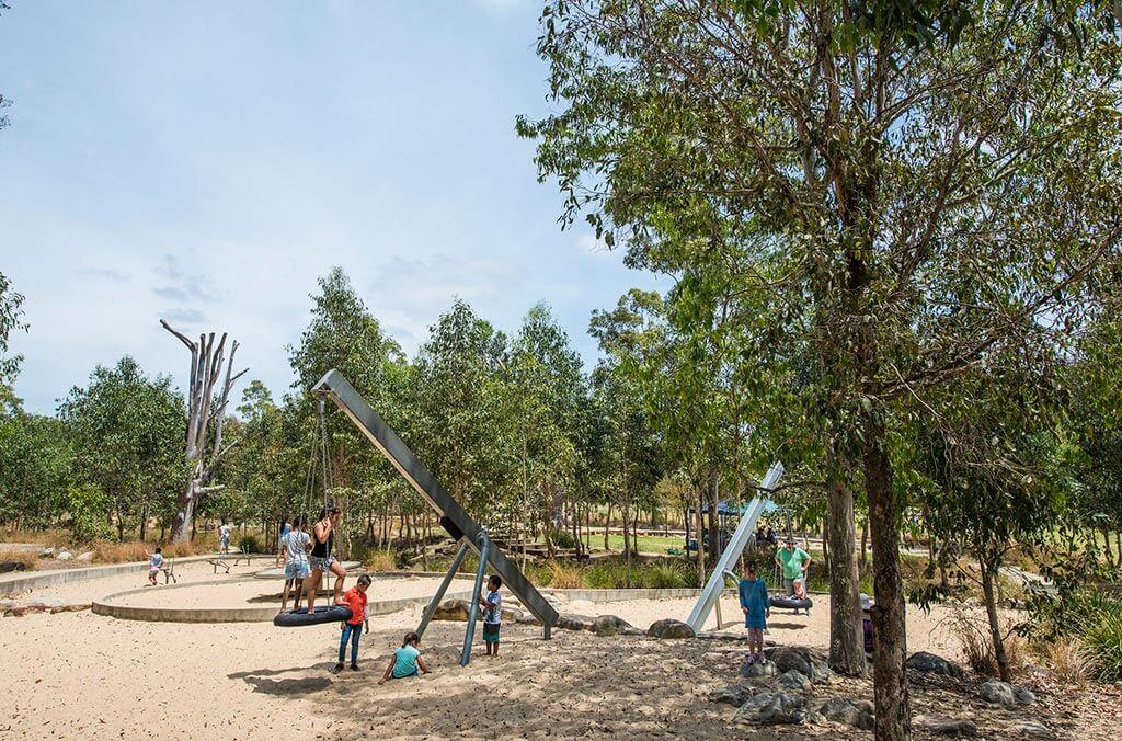 A vibrant playground filled with swings, surrounded by leafy trees, creating a fun and lively atmosphere for children.