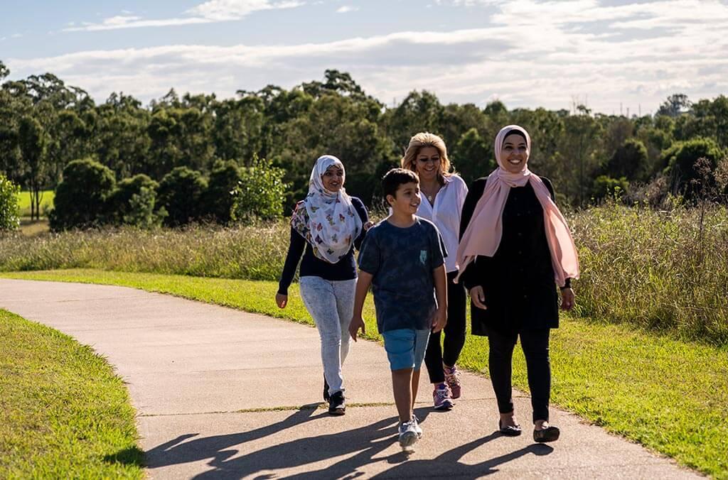 Two women and two children stroll together along a scenic path, enjoying a sunny day outdoors.