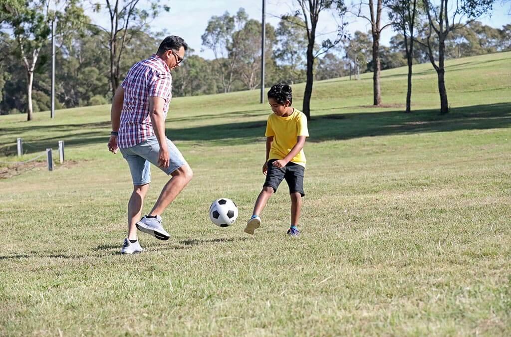 A man and a boy are playing soccer together on a sunny grassy field.