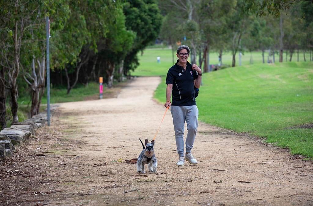 A man strolls down a path with his dog trotting beside him.