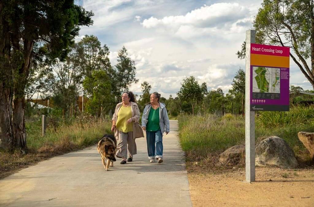 Two women stroll along the Shale Hills Loop path, walking their dog beside a sign.