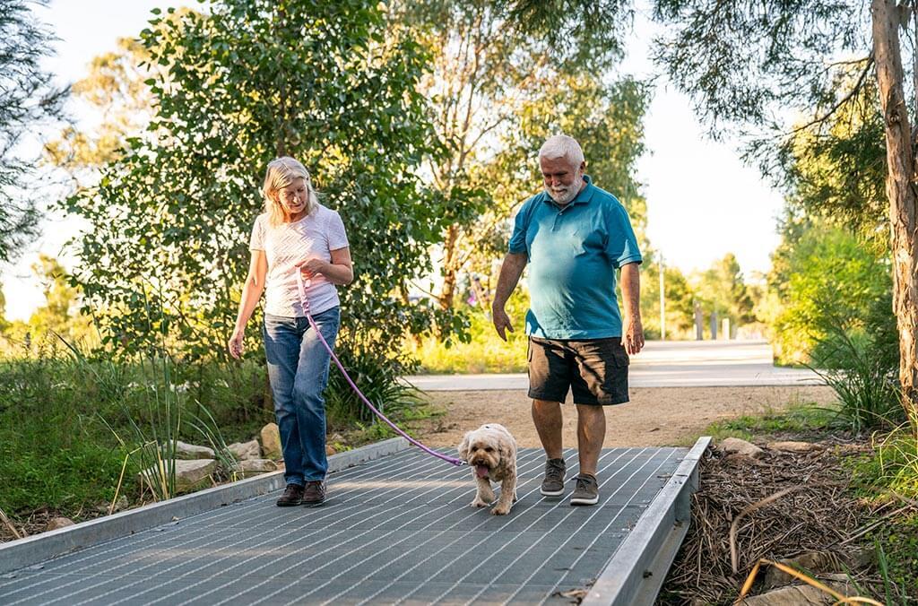 An elderly man and woman stroll with their dog on a bridge at Shale Hills Loop.